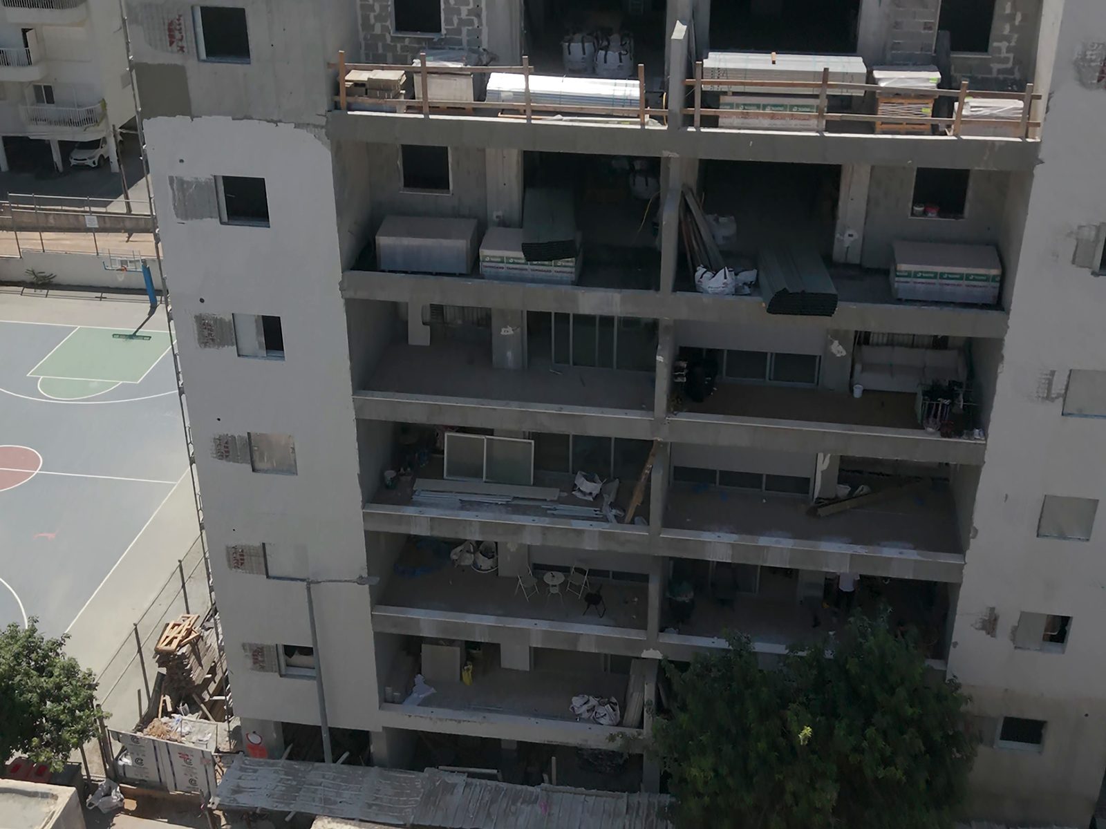 צילום רחפן של חזית בניין מגורים גבוה בשלבי בנייה, עם משטחי חומרים על הגג