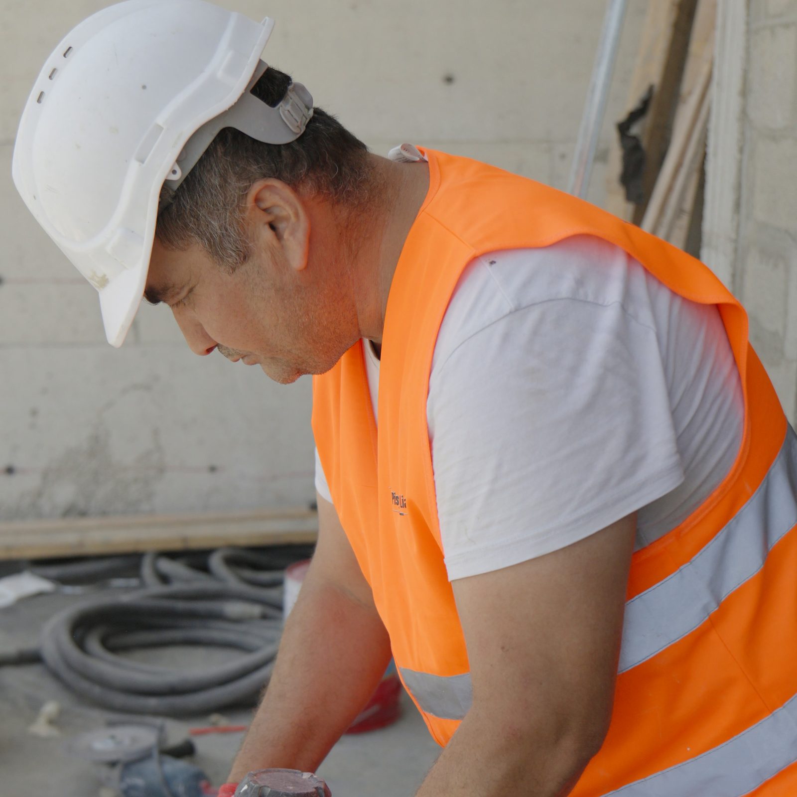 עובד בקסדה לבנה ובאפוד כתום ממותג מערבב חומר בנייה בחבית, בתוך קומת שלד