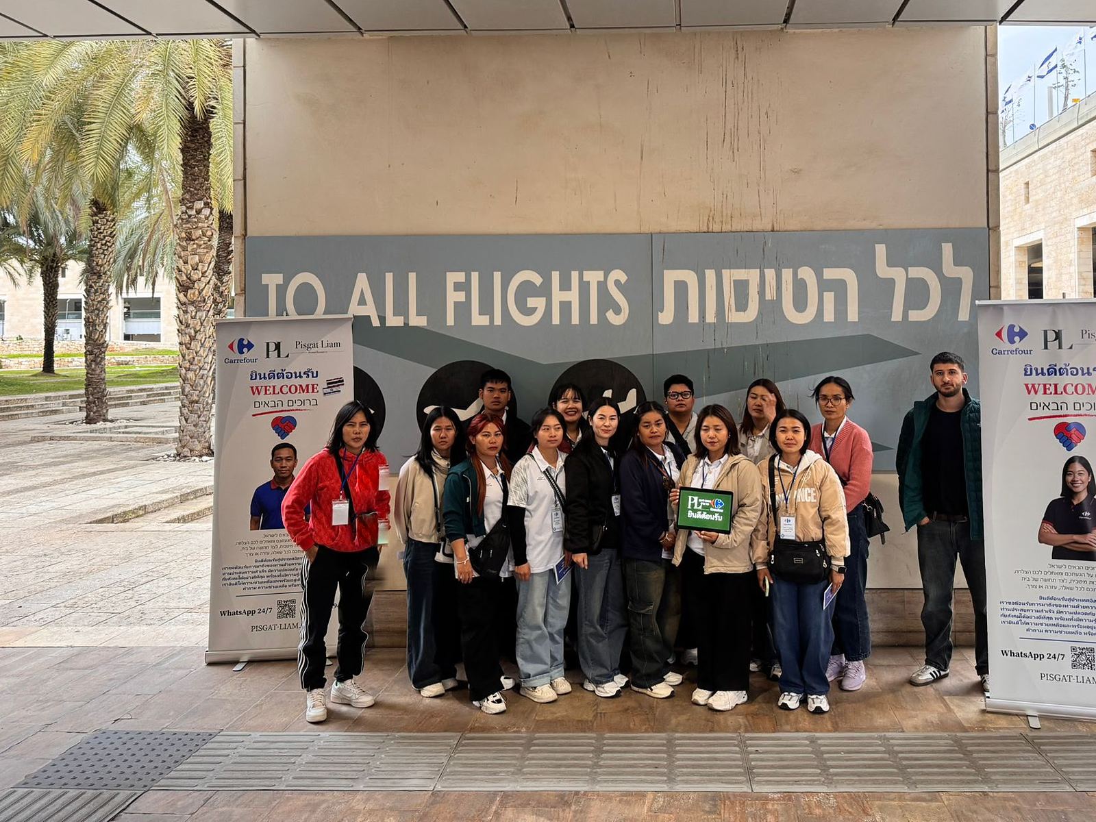 עובדות ועובדים חדשים בנמל התעופה בן גוריון לצד רול-אפים של קבלת פנים בשפת העובדים ובעברית