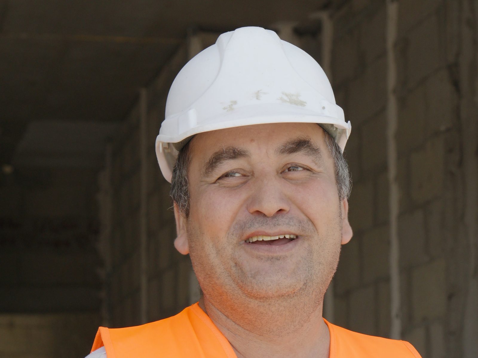 עובד בקסדה לבנה ובאפוד כתום ממותג מחייך בתוך קומת שלד עם קירות בלוקים