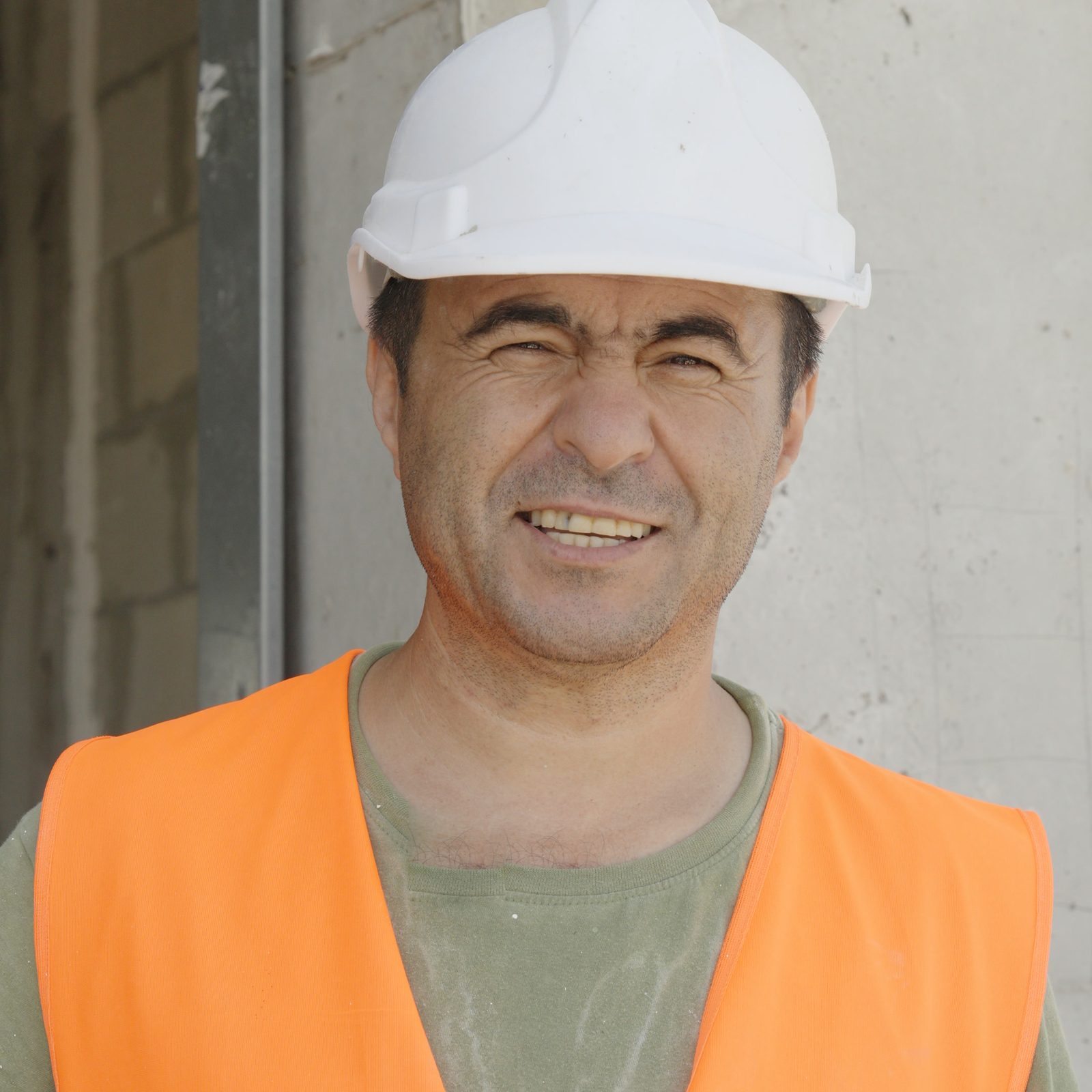 עובד בקסדה לבנה ובאפוד כתום ממותג צוחק מול המצלמה, על רקע קיר בטון