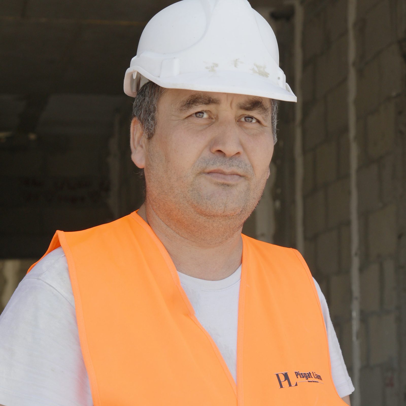 פורטרט של עובד בקסדה לבנה ובאפוד כתום ממותג בתוך מבנה בבנייה